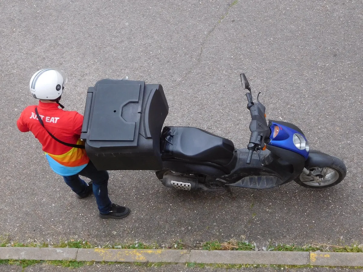 Livreur à scooter assurant une livraison à domicile devant un immeuble